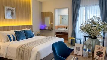 Habitación de hotel con cama, escritorio con silla, baño y vistas al exterior.