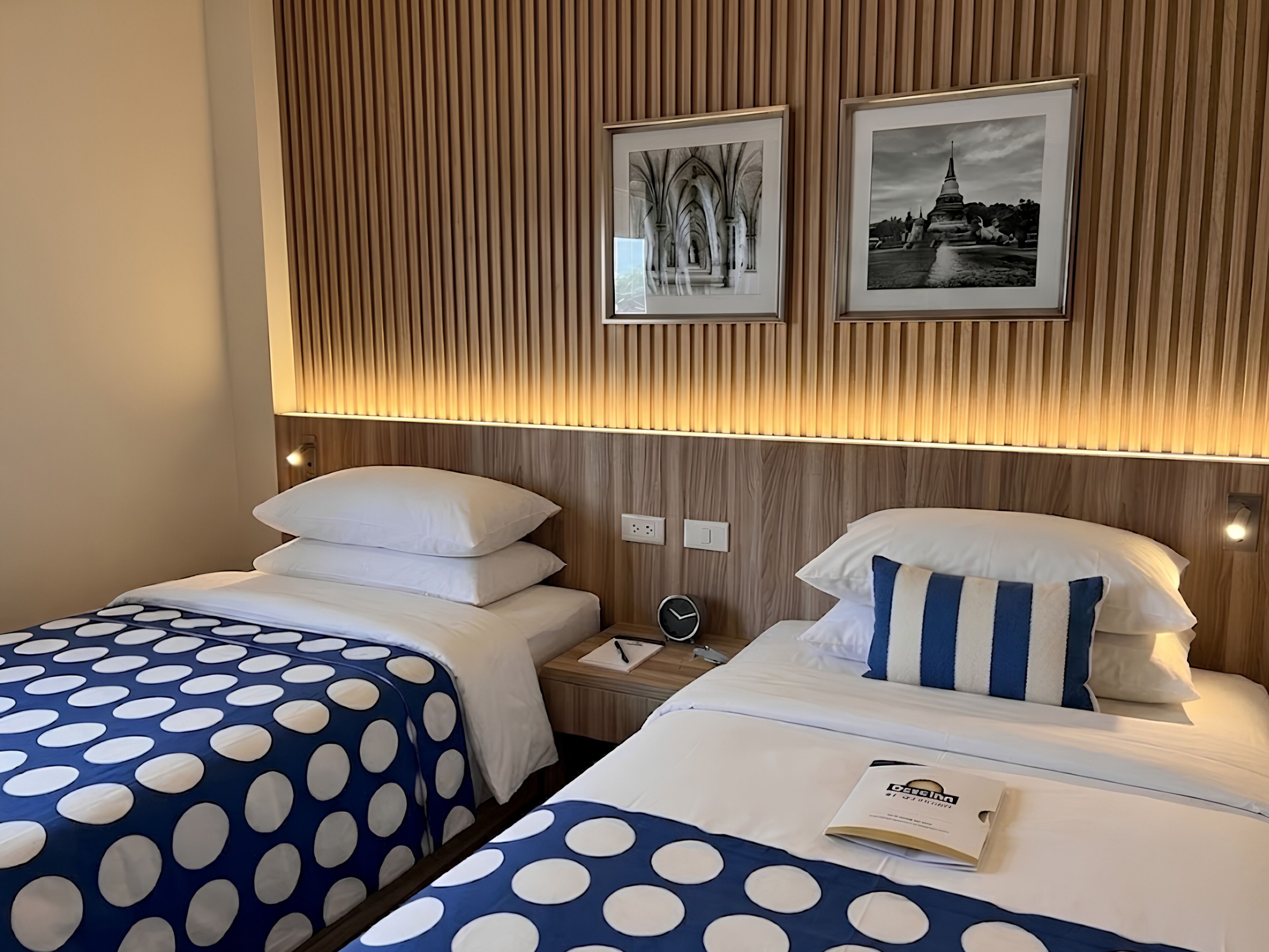 A hotel room with two beds, each with a polka dot bedspread, a wooden slat wall, and two framed pictures above the beds.