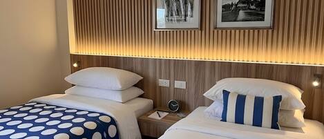 A hotel room with two beds, each with a polka dot bedspread, a wooden slat wall, and two framed pictures above the beds.