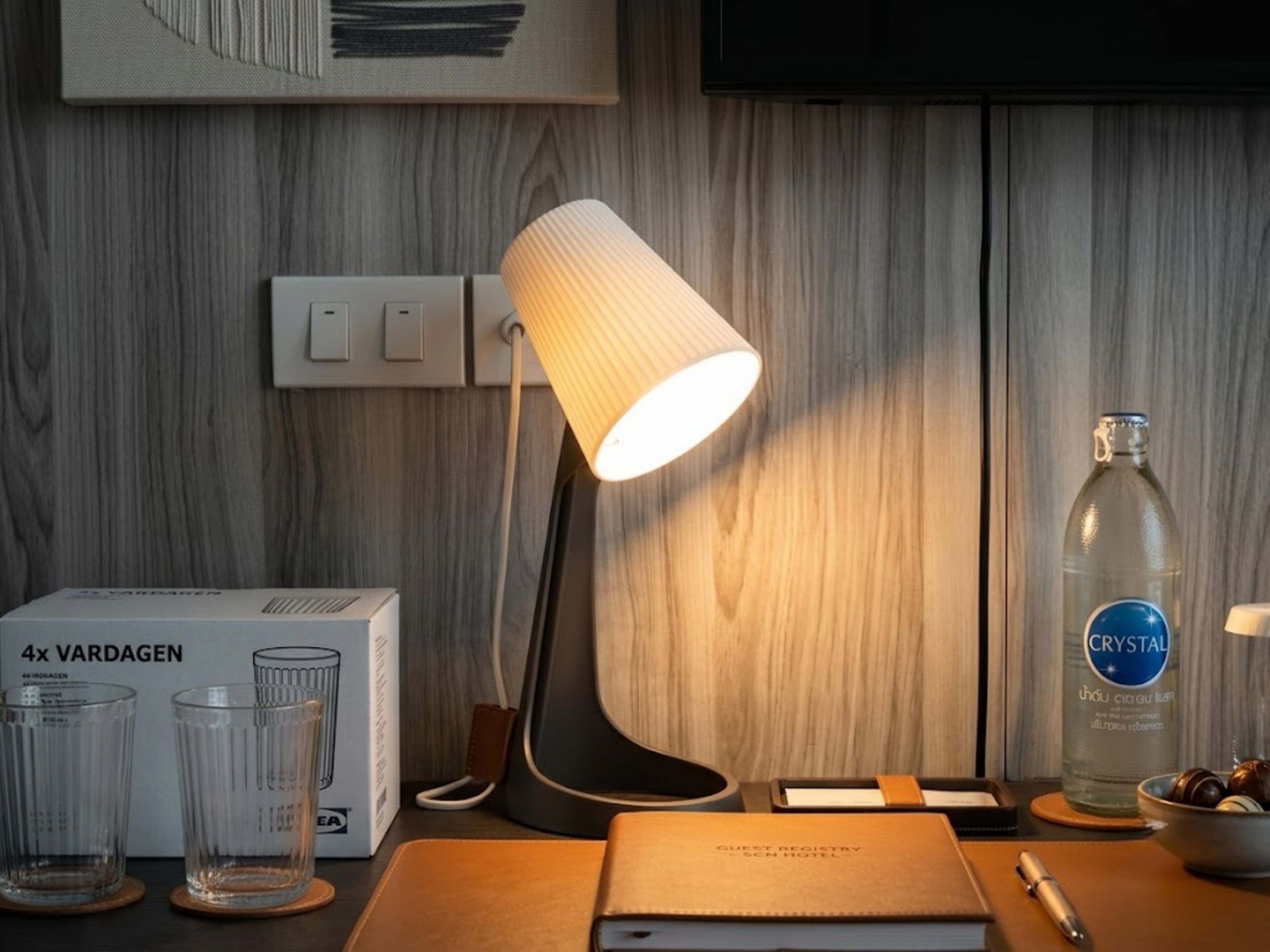 A desk with a lamp, a bottle of water, glasses, a notebook, and a pen.