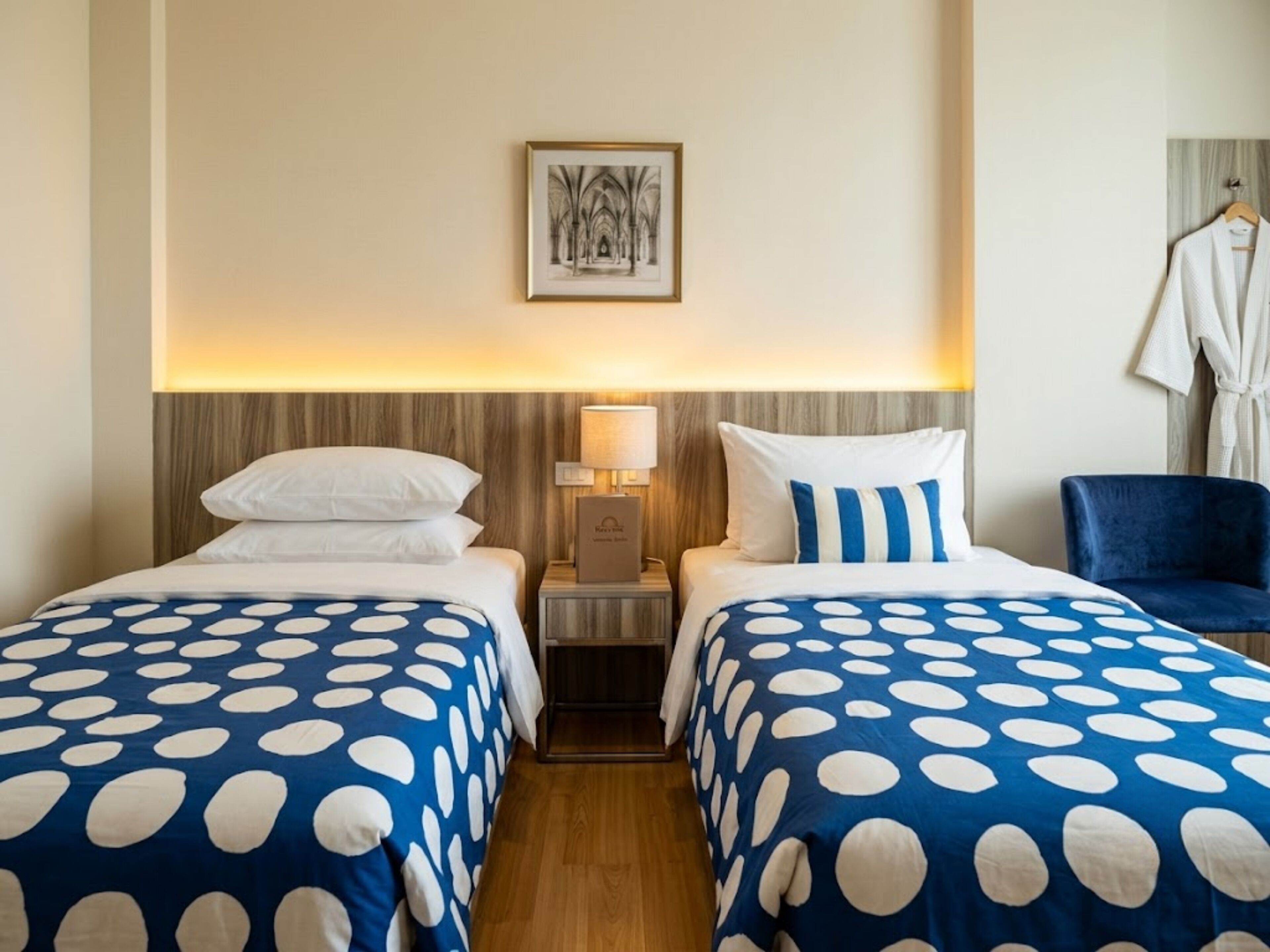 A hotel room with two beds, a nightstand, a lamp, a robe, and a chair.