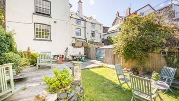 A courtyard with a wooden deck, stone wall, and green chairs.