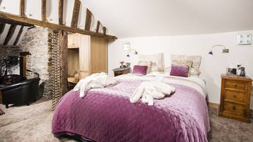 Un dormitorio con una cama grande, pared de piedra, vigas de madera, cómoda de madera y mesita de noche.