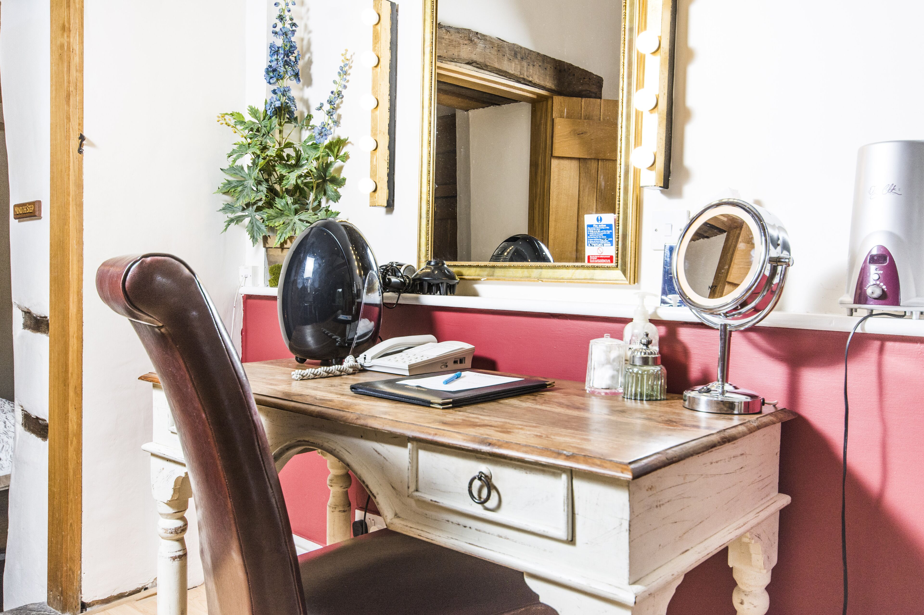 A wooden desk with a telephone, a mirror, and a hairdryer.