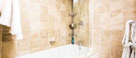 A bathroom with beige tiles, a white bathtub, and a glass-enclosed shower.