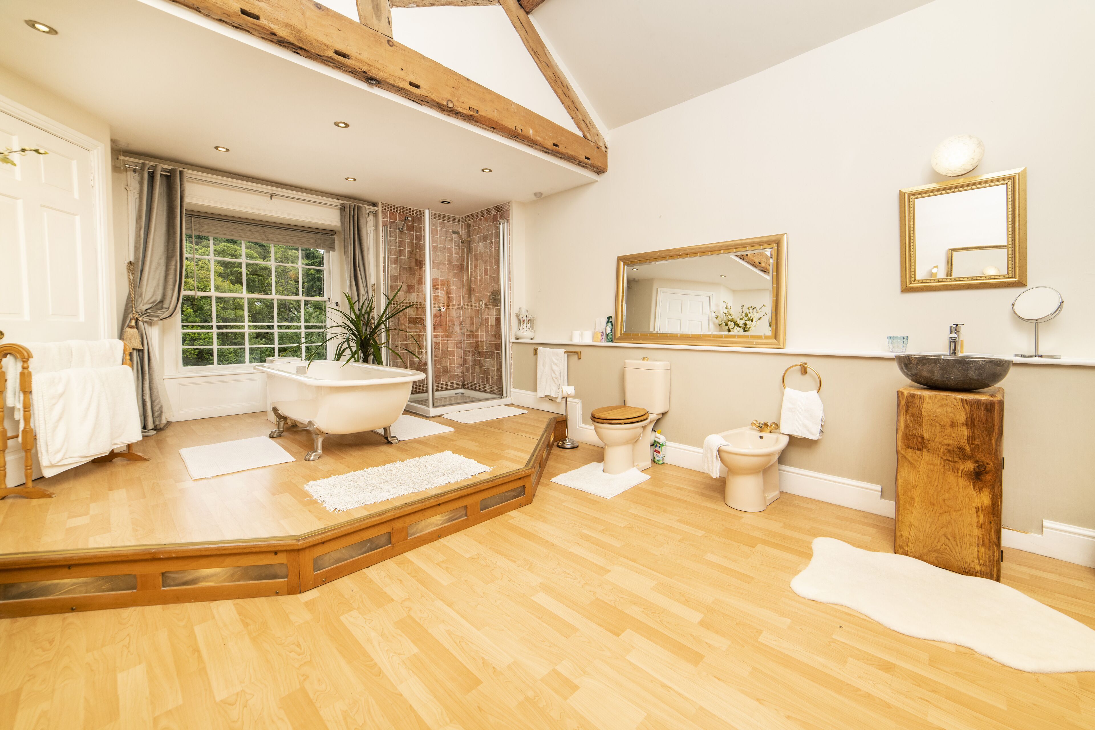 A spacious bathroom with a freestanding bathtub, a large mirror, and a wooden floor.