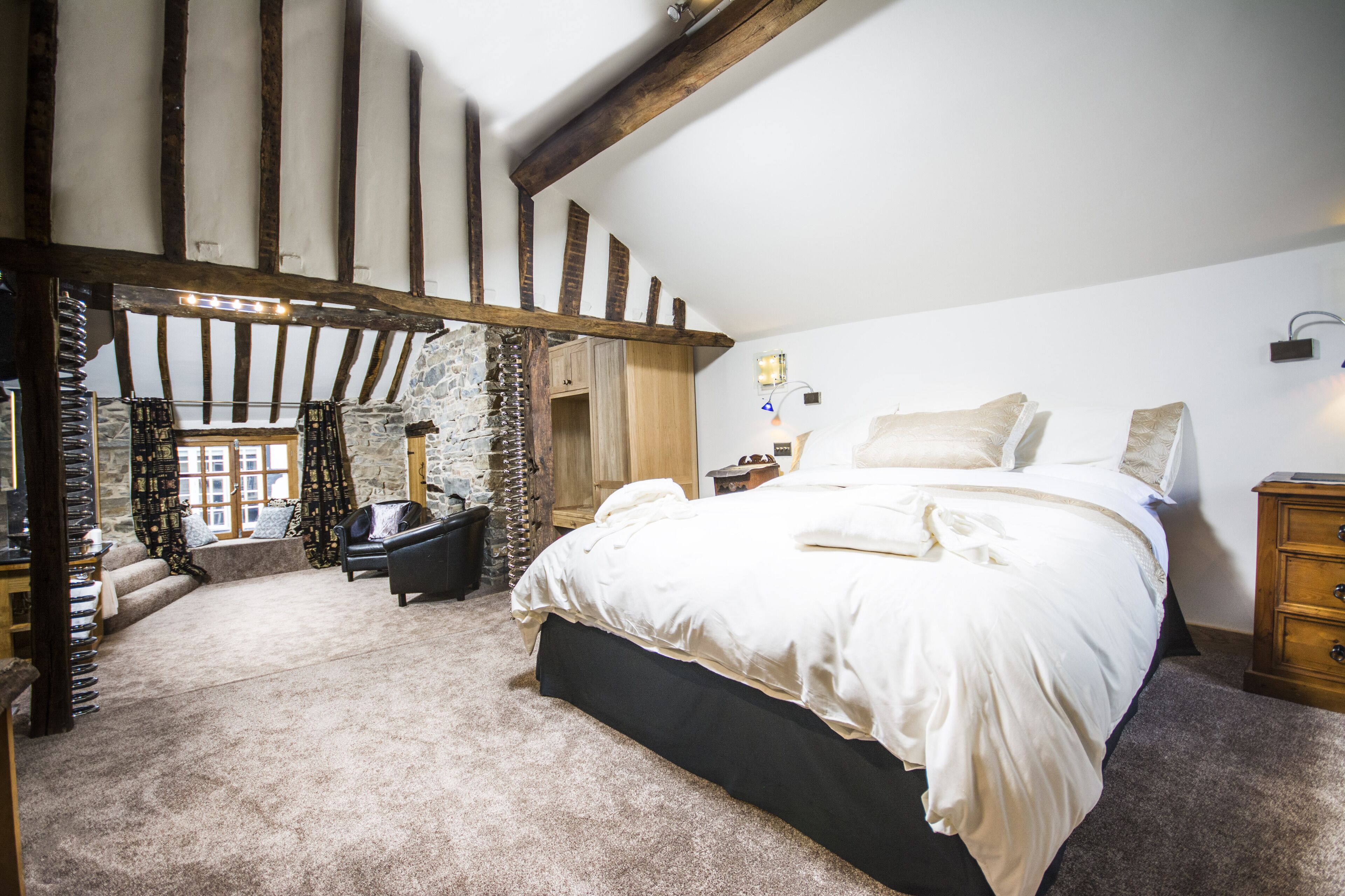 A bedroom with a large bed, a stone wall, and a wooden ceiling.