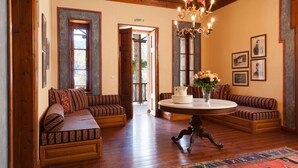 A spacious room with wooden flooring, a round table with a vase of flowers, and two patterned sofas. - The Chatzigaki Manor (Pyli)