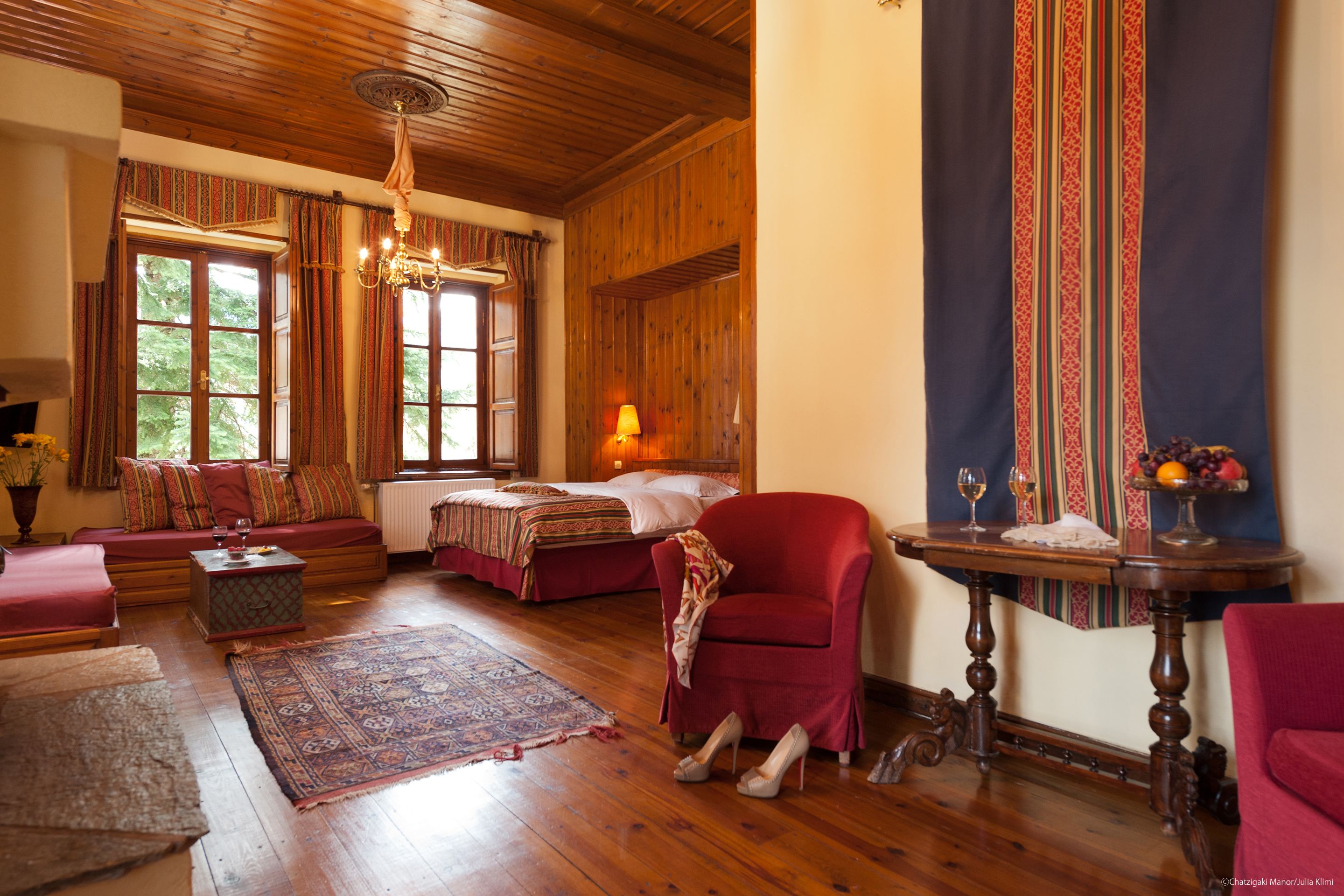 Una habitación acogedora con techo de madera, un sofá, una cama, un sillón rojo y una mesa con fruteros.