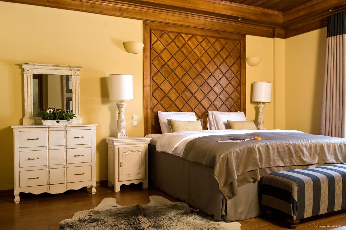 Ein Schlafzimmer mit einem Holz-Kopfteil, einer weißen Kommode mit Schubladen, Nachttischlampen, einem Bett mit Streifenmusterdecke und einem kleinen Teppich.