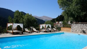 A swimming pool with four wooden loungers, each with a canopy. There are stone walls and a wooden fence surrounding the pool. - The Chatzigaki Manor (Pyli)