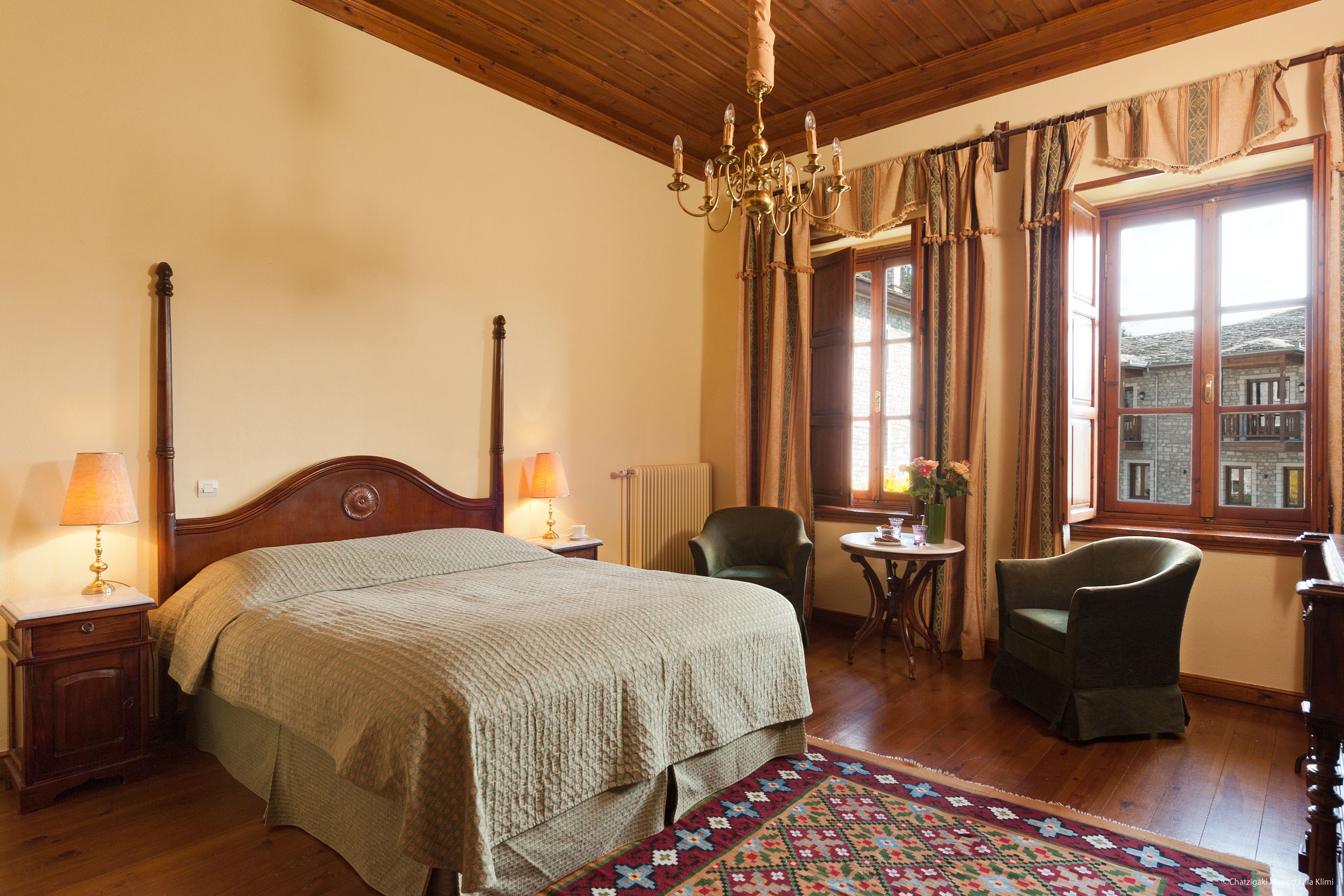 A hotel room with a large bed, two chairs, a small table, and a window with curtains.