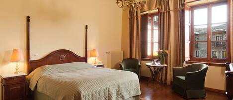 A hotel room with a large bed, two chairs, a small table, and a window with curtains.