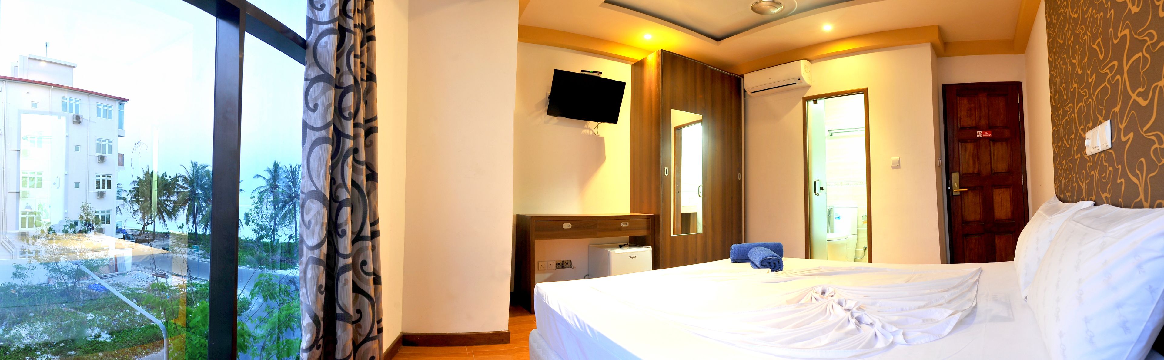 Habitación de hotel con cama, televisor, espejo y ventana con cortinas.