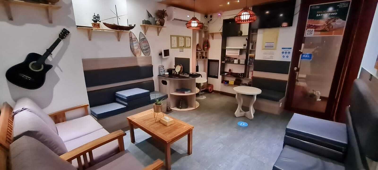 A cozy room with a sofa, a wooden table, and a guitar. There are shelves with decorative items and a door with a 'FULL' sign.