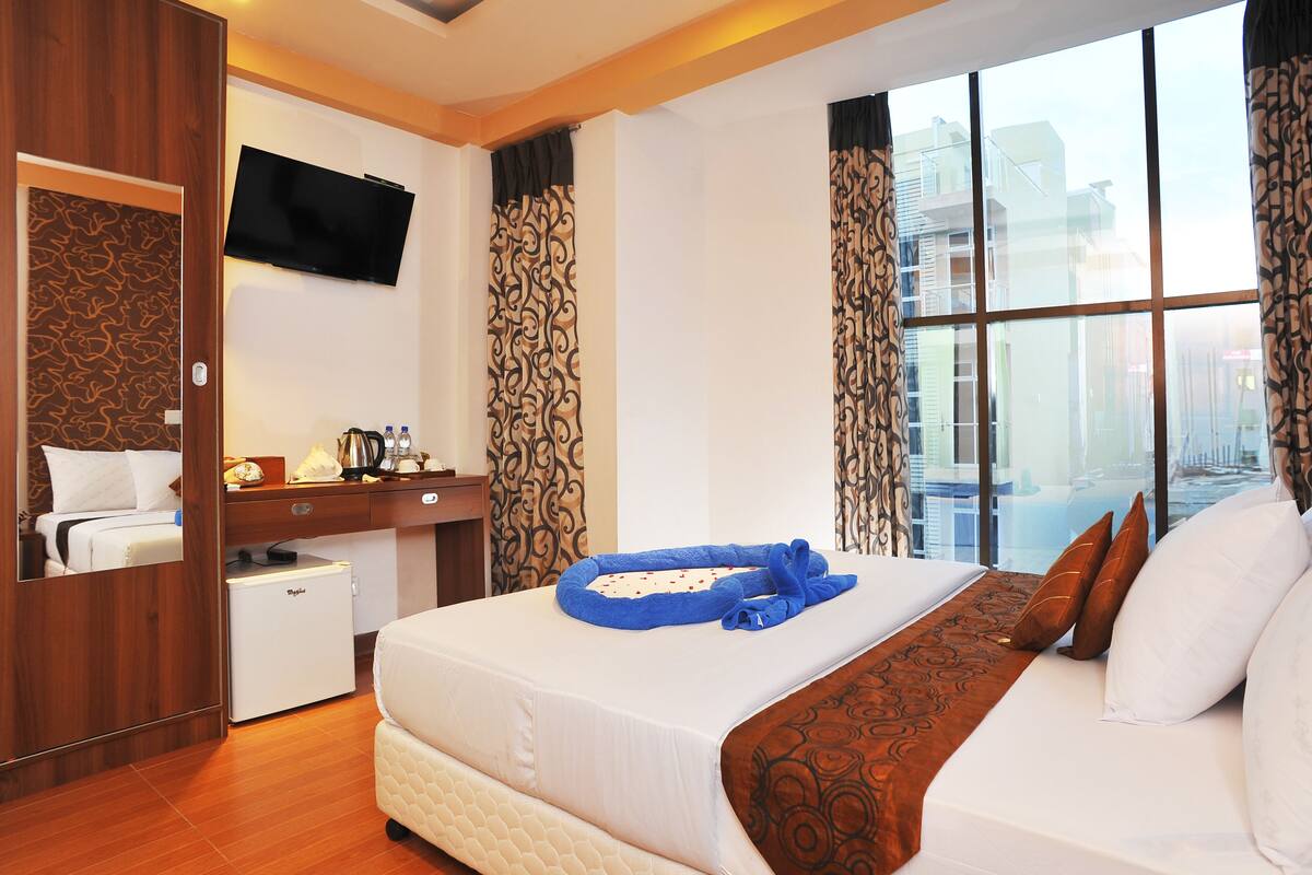 A hotel room with a bed, a desk, a television, and a view of the city.