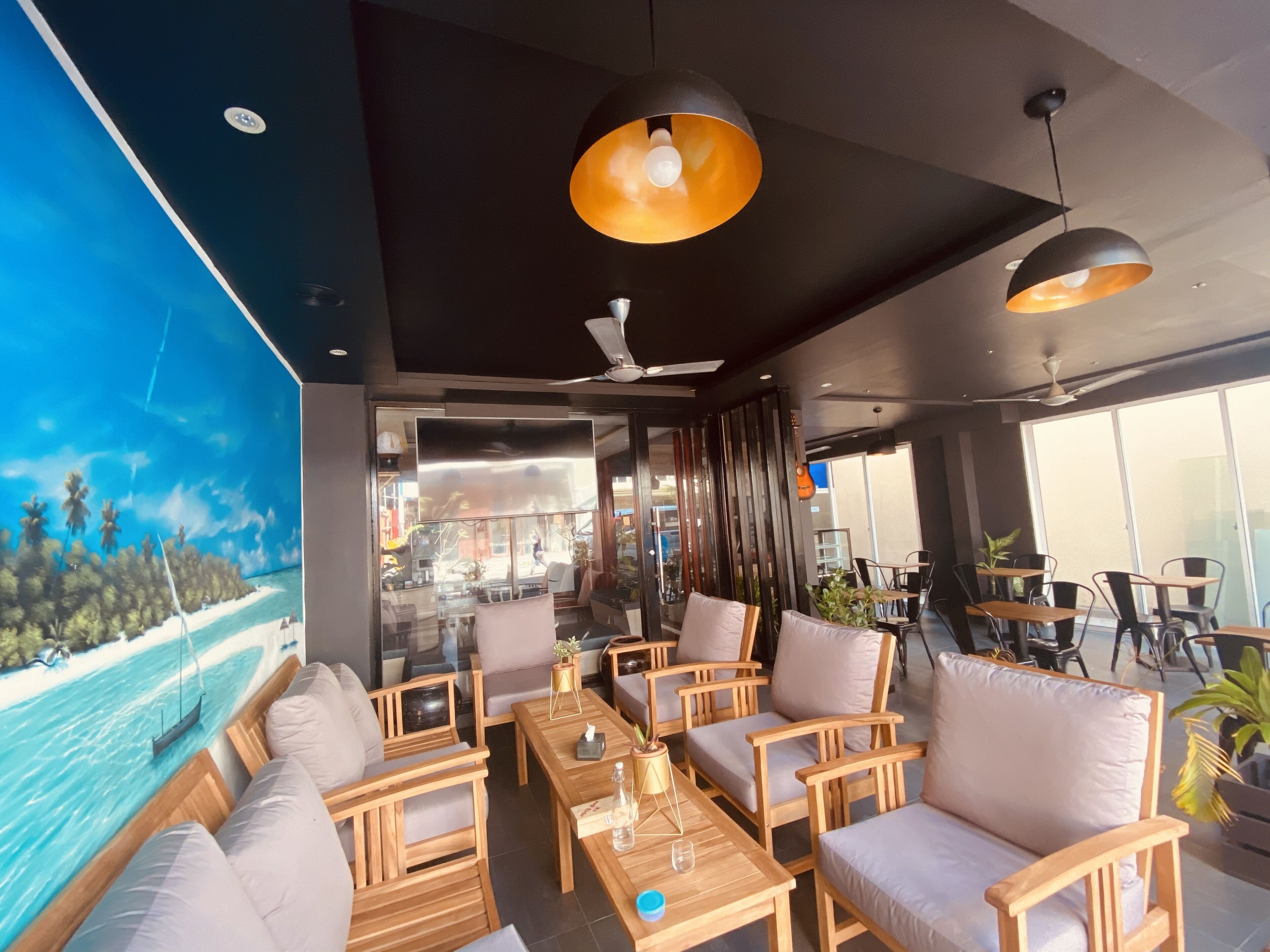 A modern lounge area with wooden furniture, a ceiling fan, and a large window with a view of a beach.