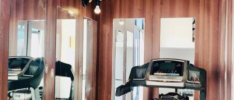 A room with wooden walls and mirrored doors, a treadmill, and a stationary bike.