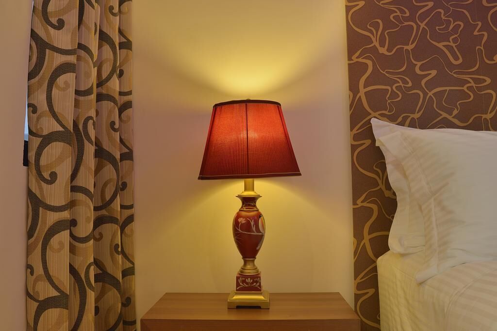 A lamp on a bedside table next to a bed with patterned wallpaper.
