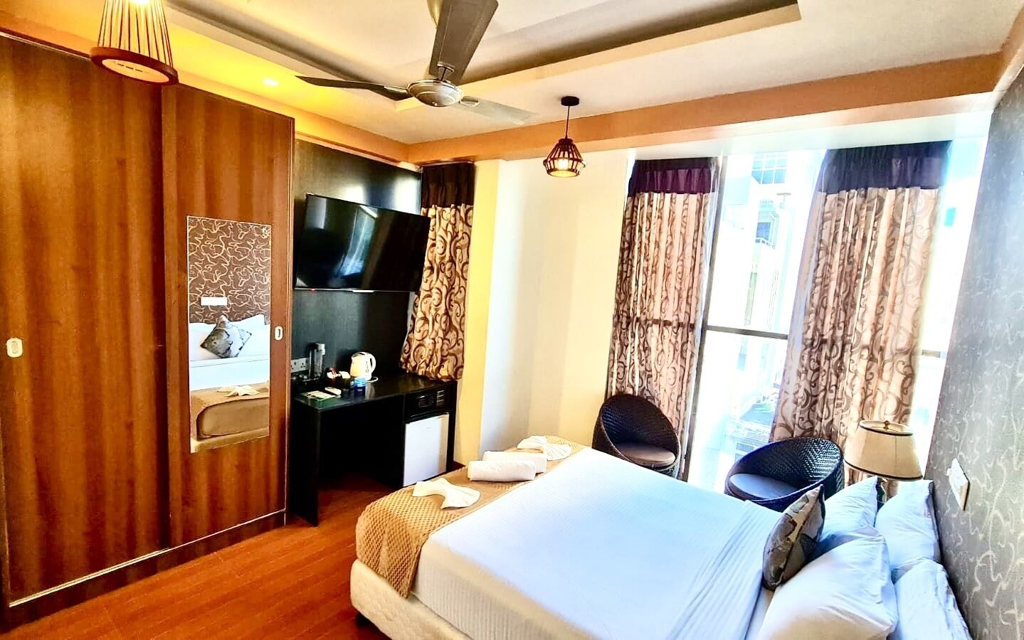 Habitación de hotel con cama, escritorio con televisor, silla y ventana con cortinas.