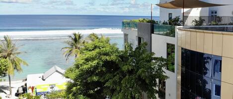Vista costera con playa, palmeras y un edificio moderno con balcón con vista al océano.