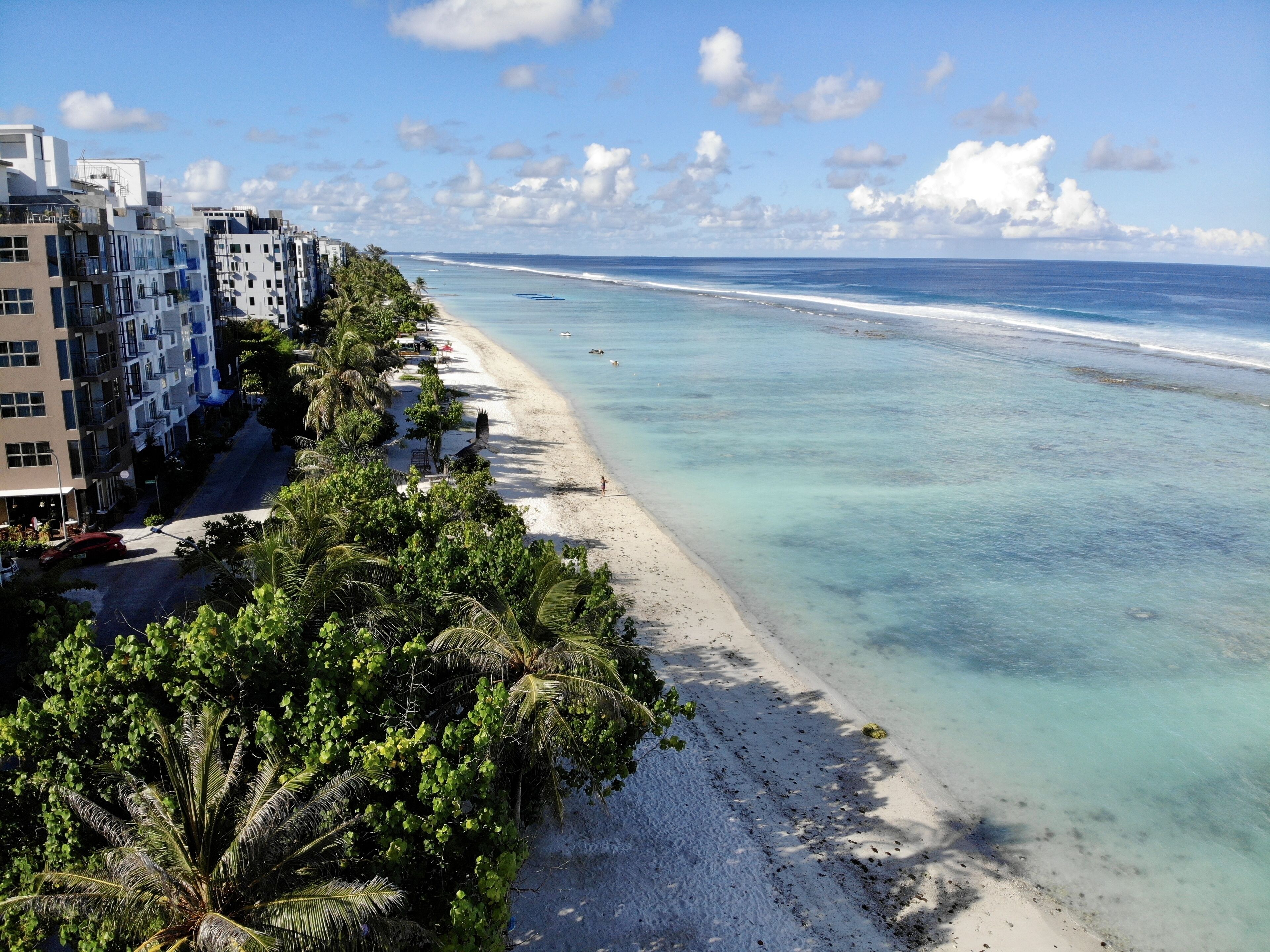 A beach with clear turquoise water, a sandy shore, and a row of modern buildings with balconies overlooking the beach.