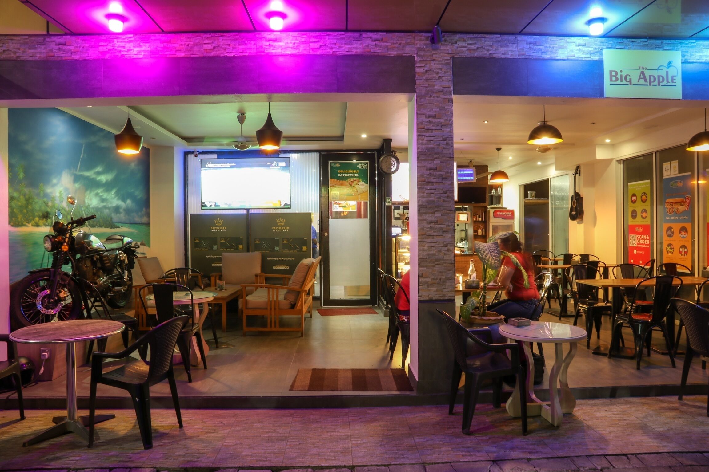 Un café interior con mesas y sillas, una motocicleta y un letrero que dice 'The Big Apple'.