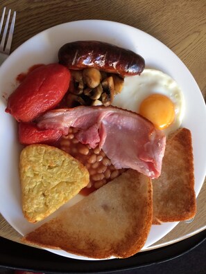 Une assiette de nourriture pour le petit-déjeuner comprenant des saucisses, des œufs, des haricots, du bacon, des toasts et des tomates.