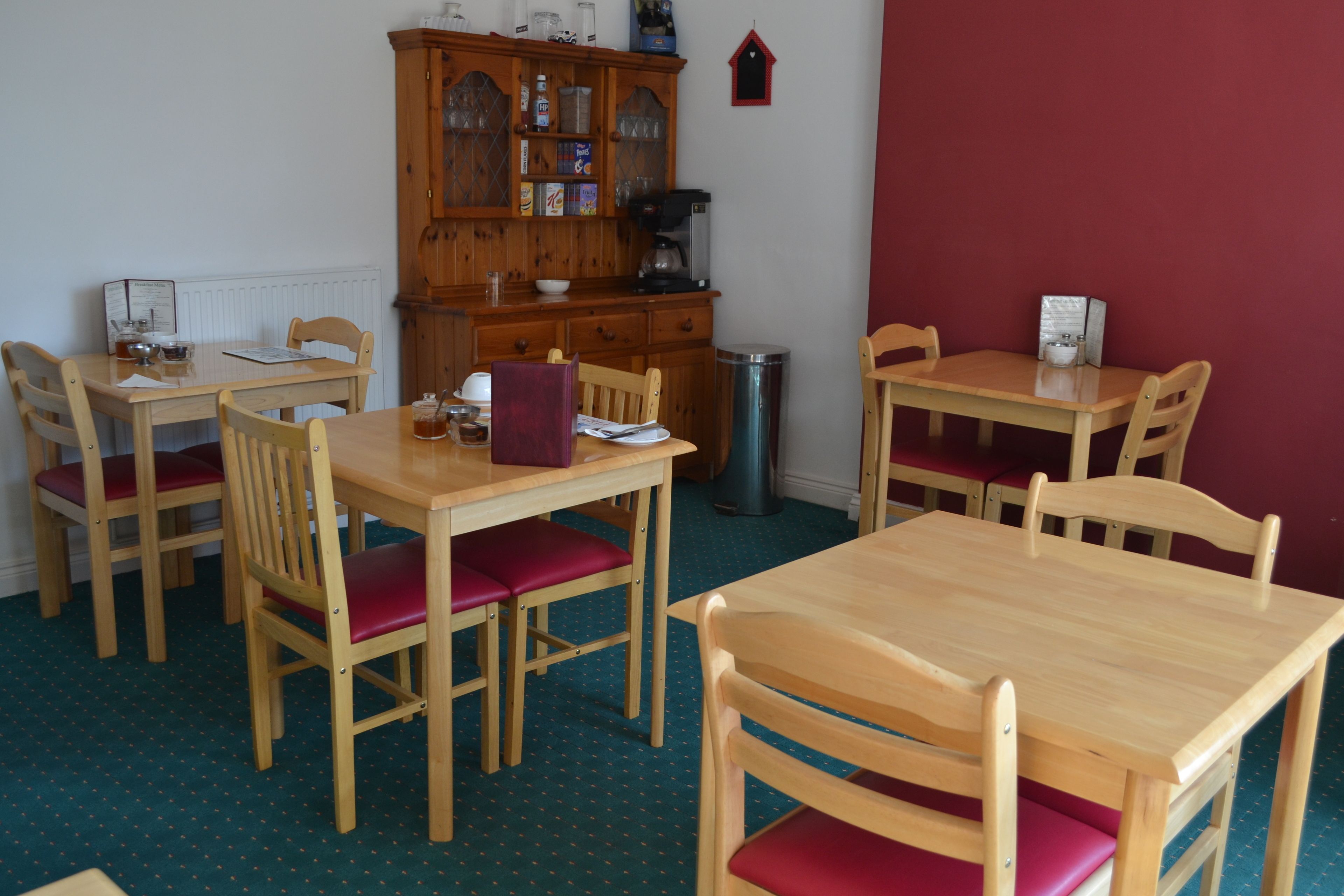 A dining area with wooden tables and chairs, a cabinet with glass doors, and a radiator.