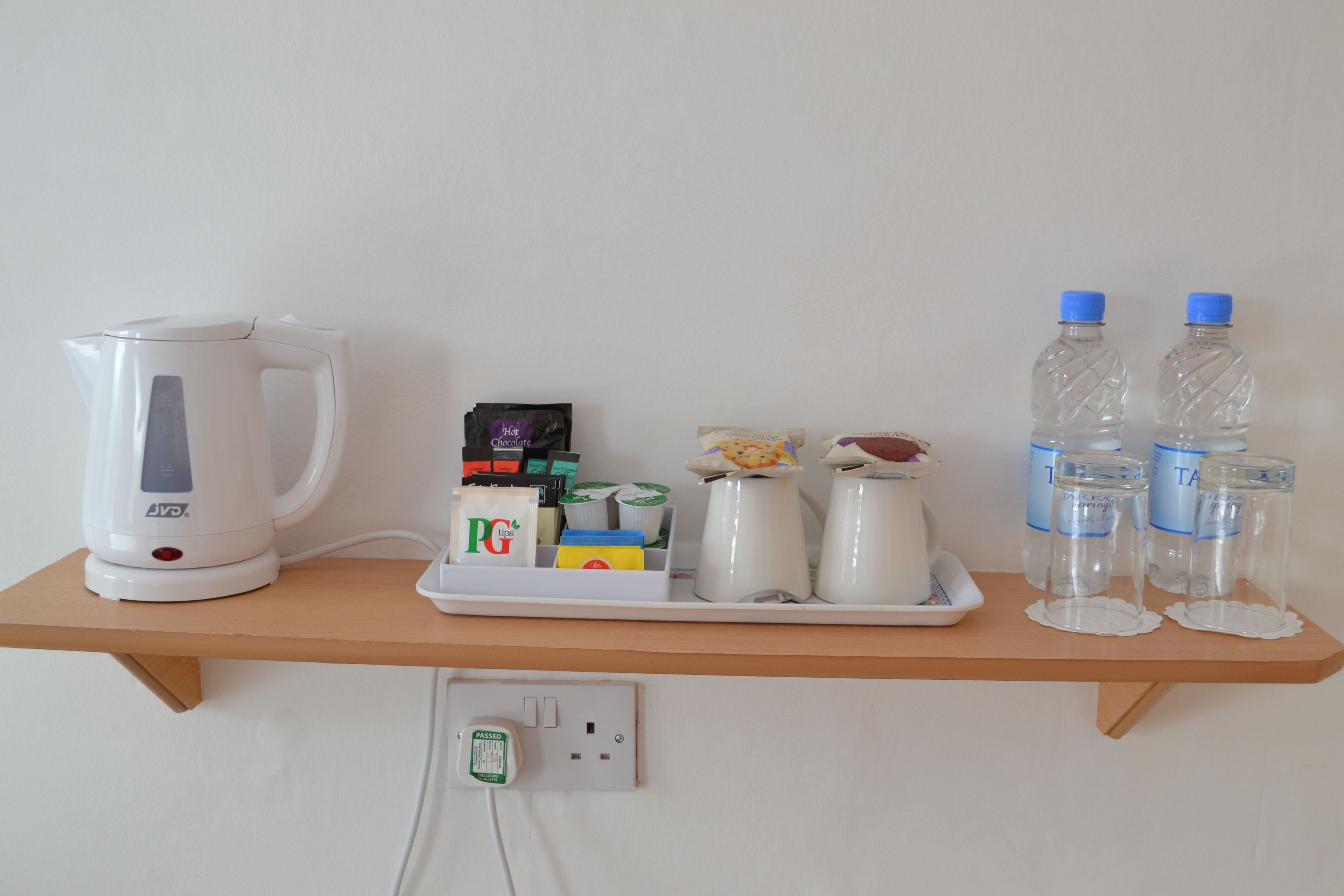 A kitchen counter with a coffee maker, tea bags, a kettle, and water bottles.