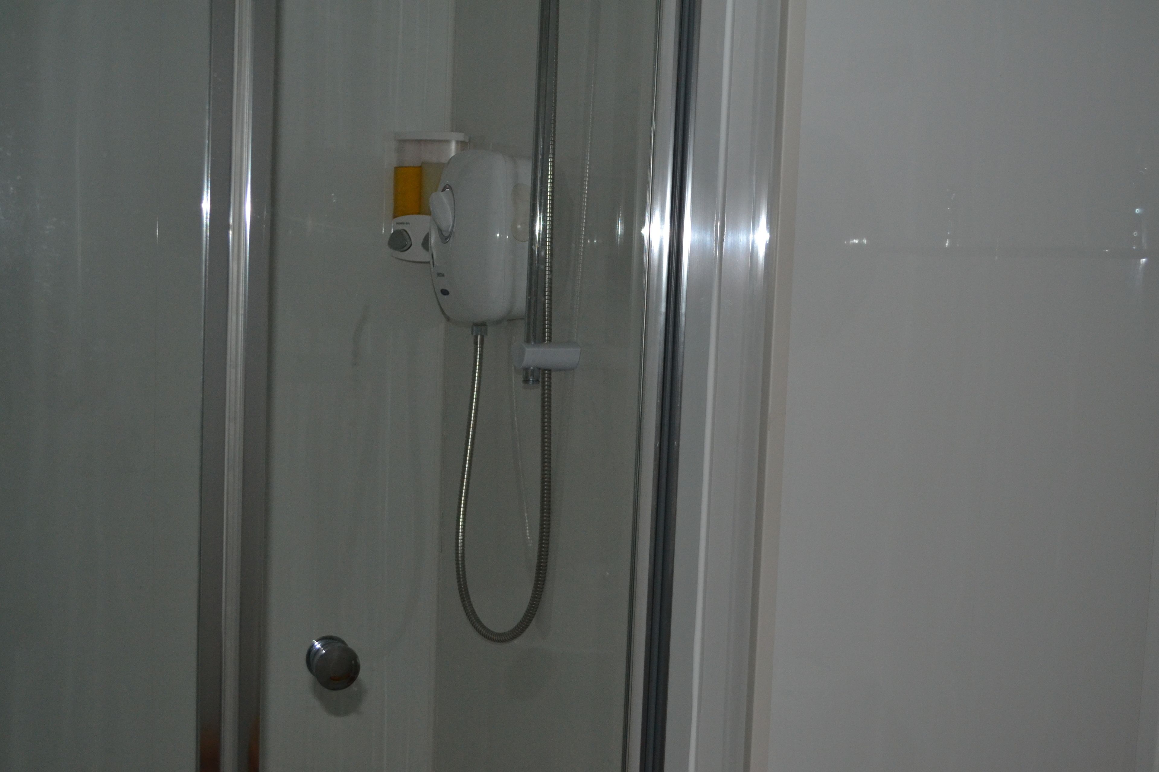 A shower area with a handheld showerhead and a wall-mounted control panel.