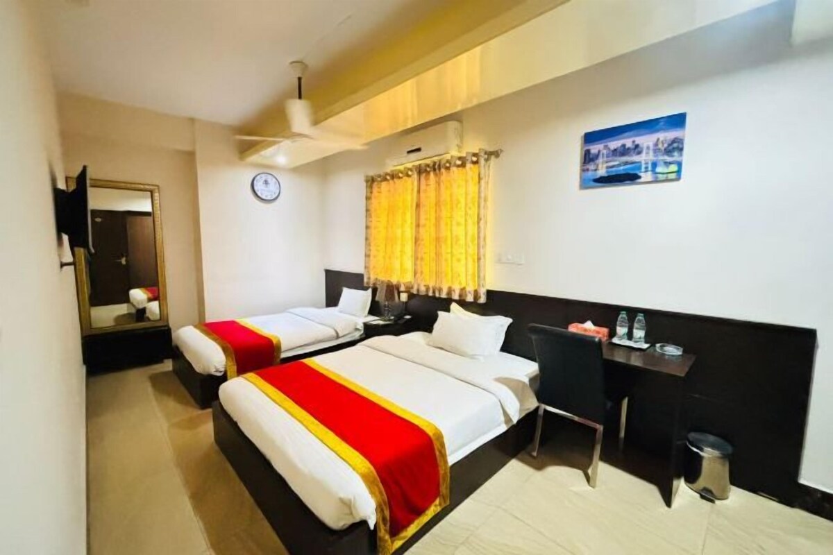 A hotel room with two beds, a desk, a chair, a trash bin, a clock, and a painting on the wall.