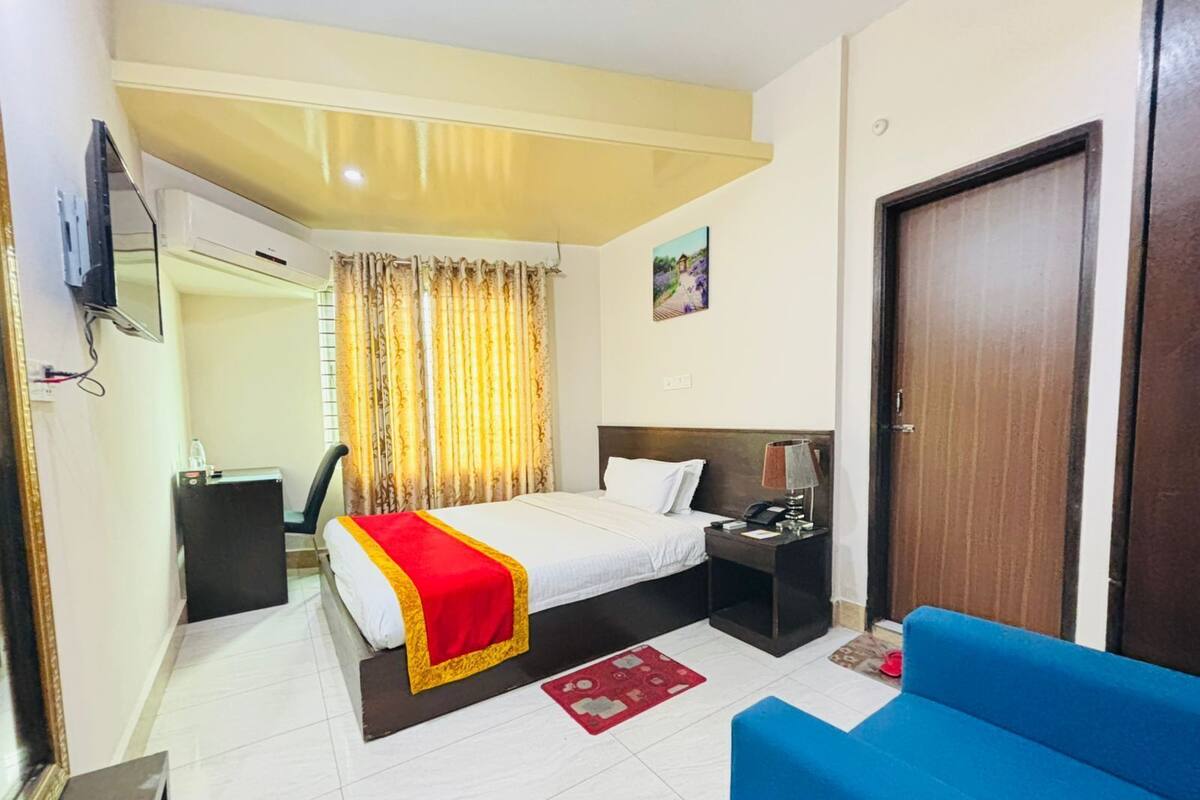 A hotel room with a bed, bedside table, lamp, and a blue sofa.