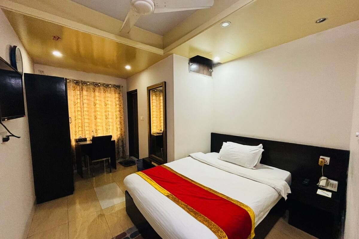 A hotel room with a bed, a desk, a chair, a wardrobe, and a mirror.