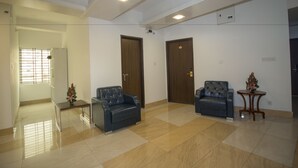 Um quarto espaçoso com piso de azulejos, dois sofás de couro, uma mesinha com um vaso e uma porta com fechadura.