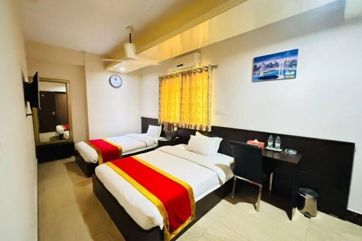 A hotel room with two beds, a desk, a chair, a trash bin, a clock, and a painting on the wall.