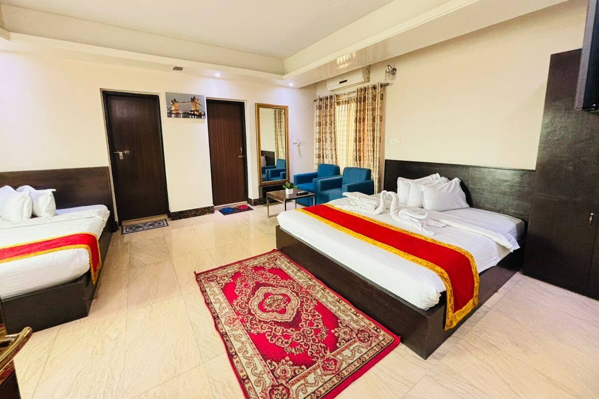 A hotel room with two beds, a red and gold patterned rug, a mirror, a blue chair, and a small table.