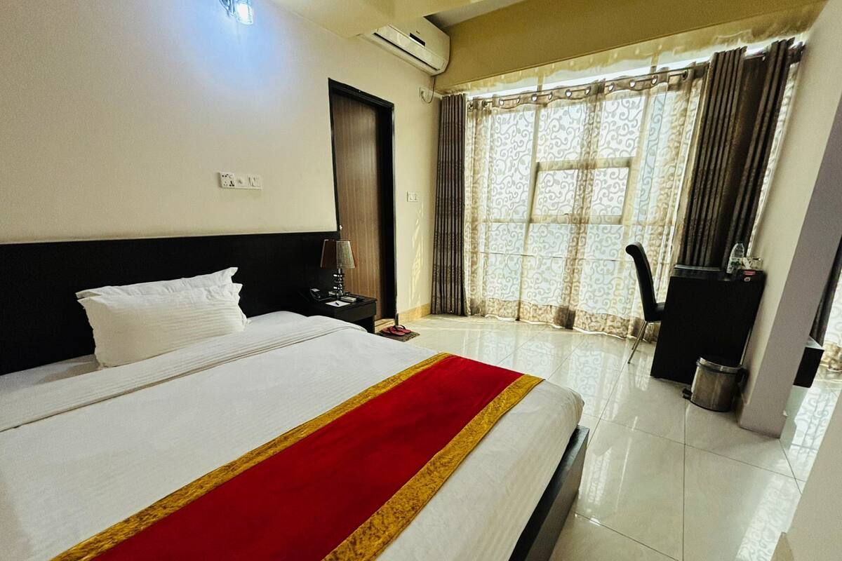 A hotel room with a bed, a nightstand, a desk, a chair, and a window with curtains.