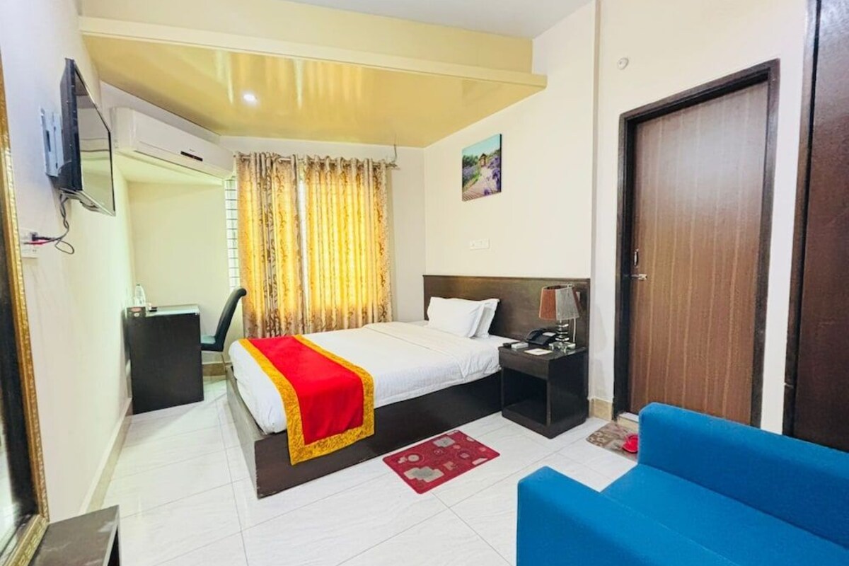 A hotel room with a bed, bedside table, lamp, and a blue sofa.