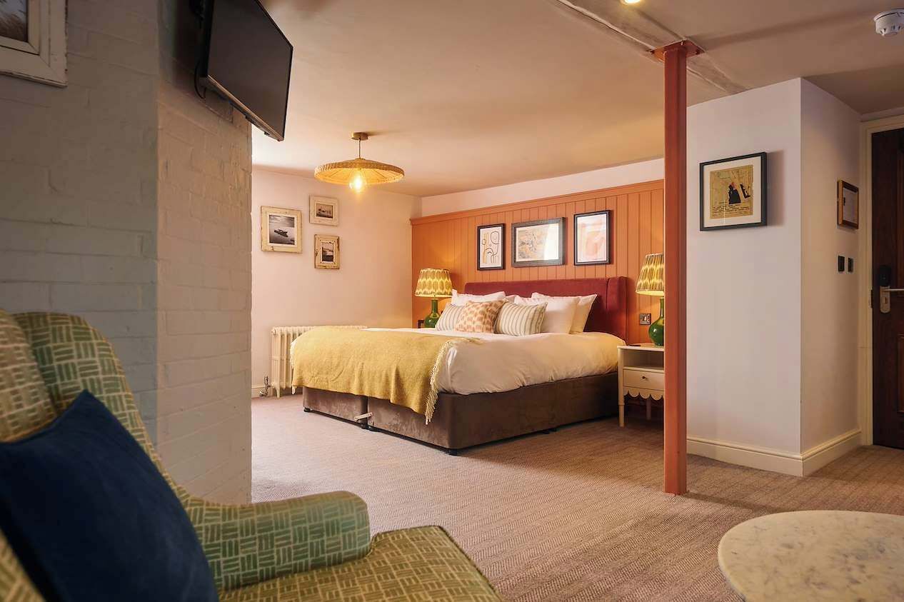 Ein Schlafzimmer mit einem Bett, Nachttischen, einer Lampe und einem an der Wand befestigten Fernseher.