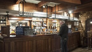 A bar with wooden paneling, a counter with a menu, and shelves with bottles and glasses. - Mill on the Exe (Exeter)