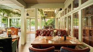 A restaurant with a wooden table set for dining, leather seating, and large windows offering a view of greenery. - Mill on the Exe (Exeter)