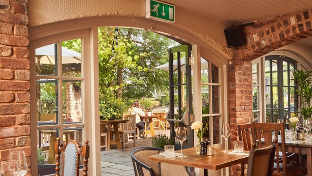 An outdoor dining area with brick walls, wooden tables, and chairs. - Mill on the Exe (Exeter)