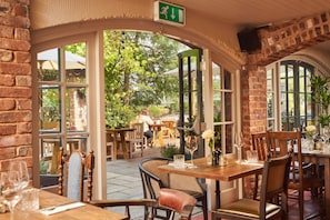 An outdoor dining area with brick walls, wooden tables, and chairs. - Mill on the Exe (Exeter)