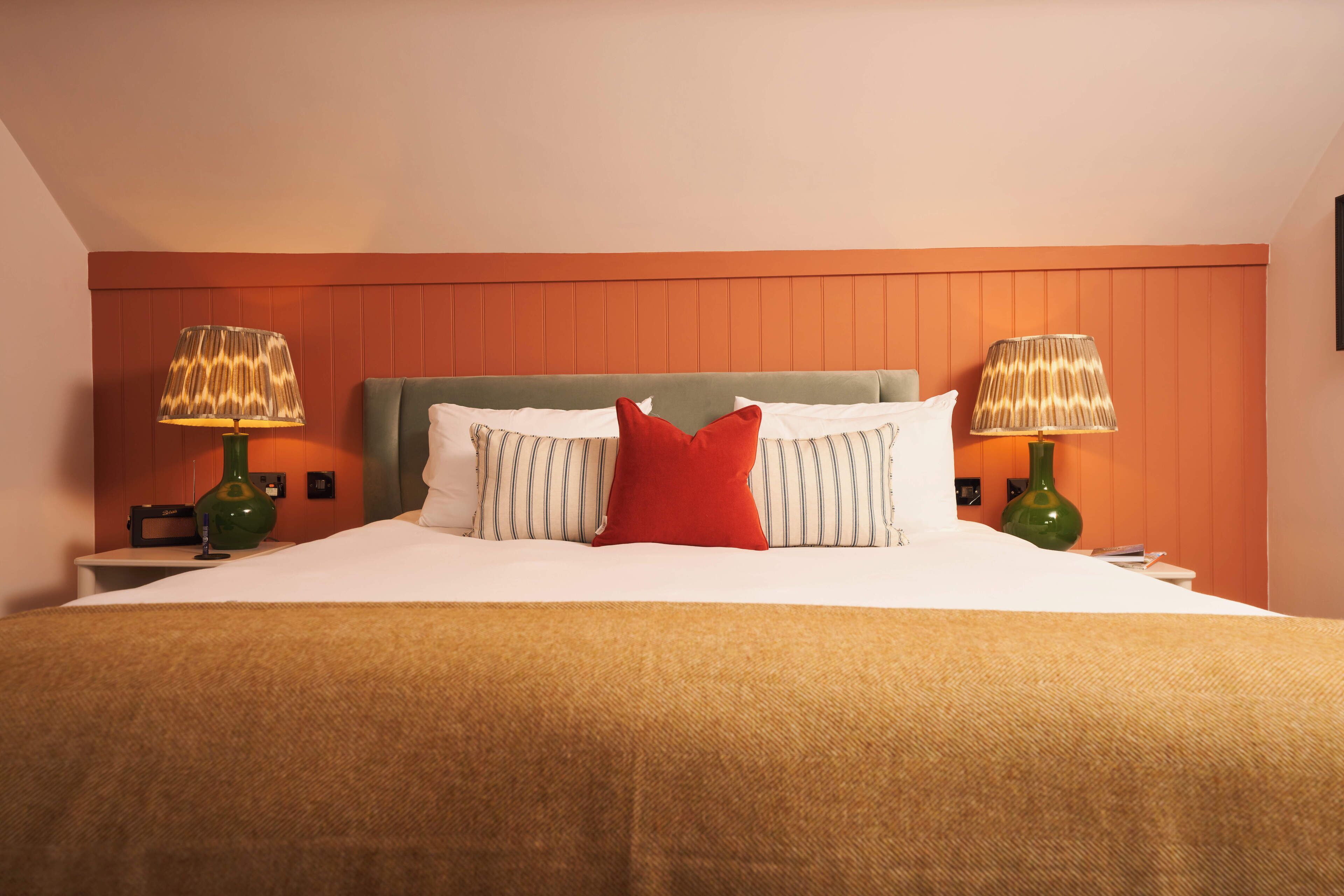 A neatly made bed with a green headboard, two bedside lamps, and a red pillow.
