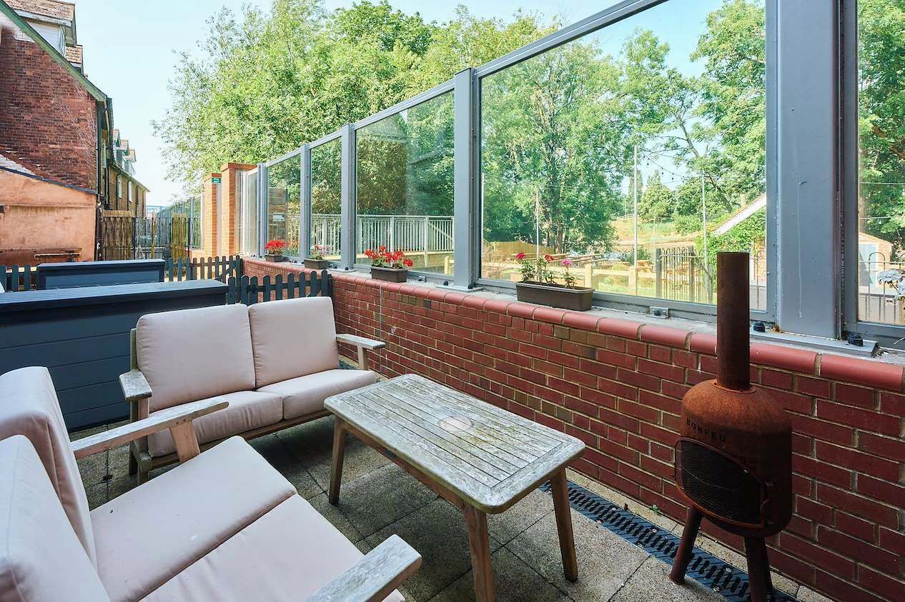 An outdoor seating area with a brick wall, a wooden table, and a barbecue grill.