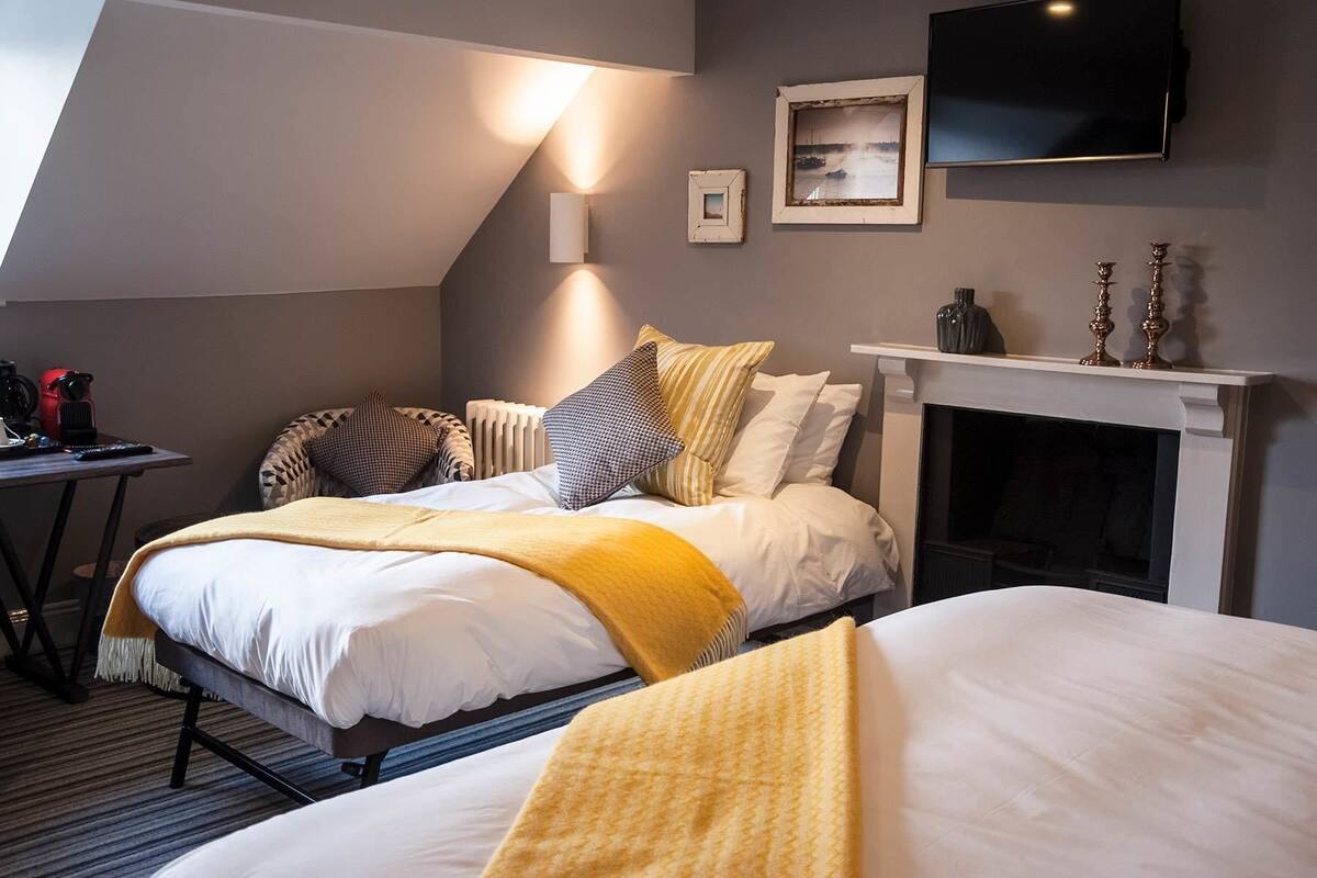 A hotel room with a bed, a fireplace, a TV, and a framed picture on the wall.