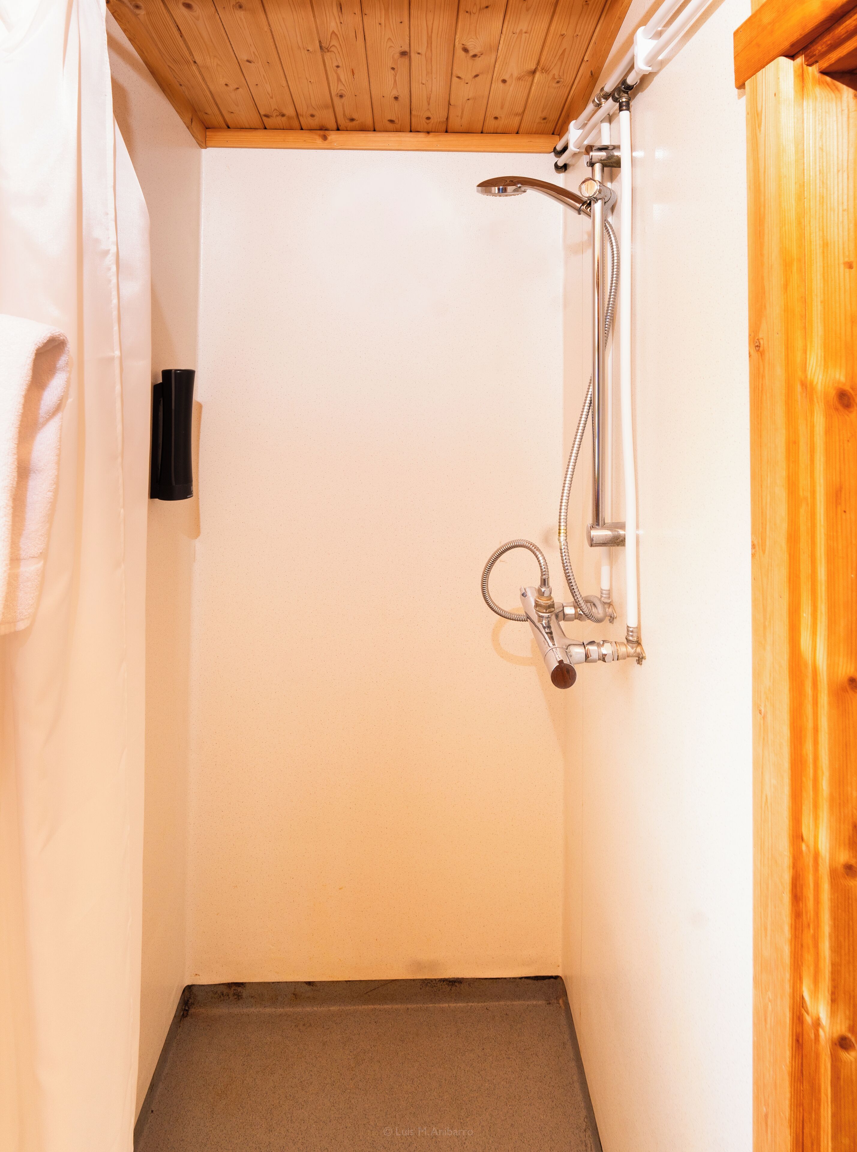 Un petit espace douche fermé, avec un plafond en bois et des murs blancs.