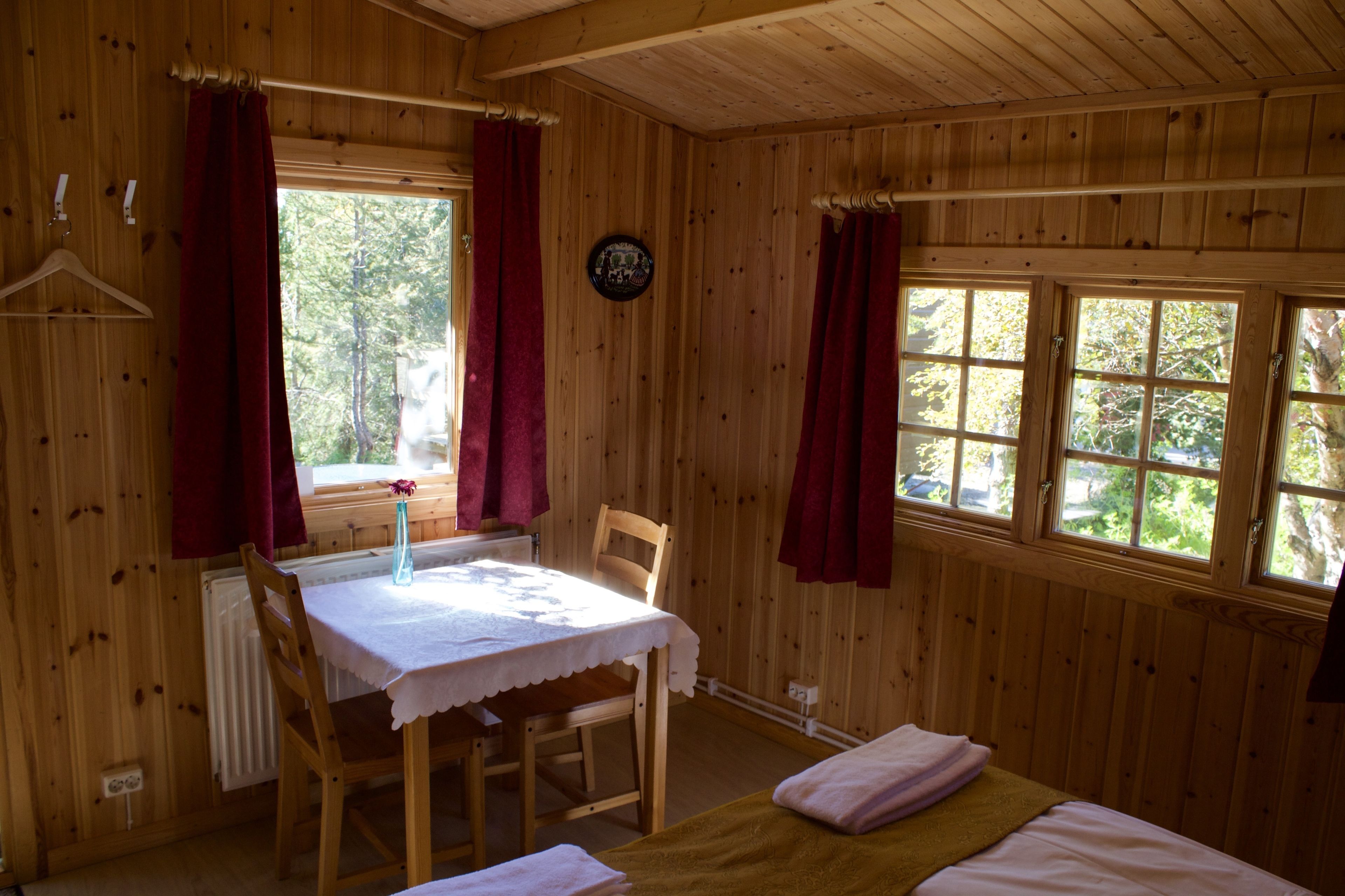 Una cabaña de madera con mesa de comedor, dos camas y ventanas grandes.