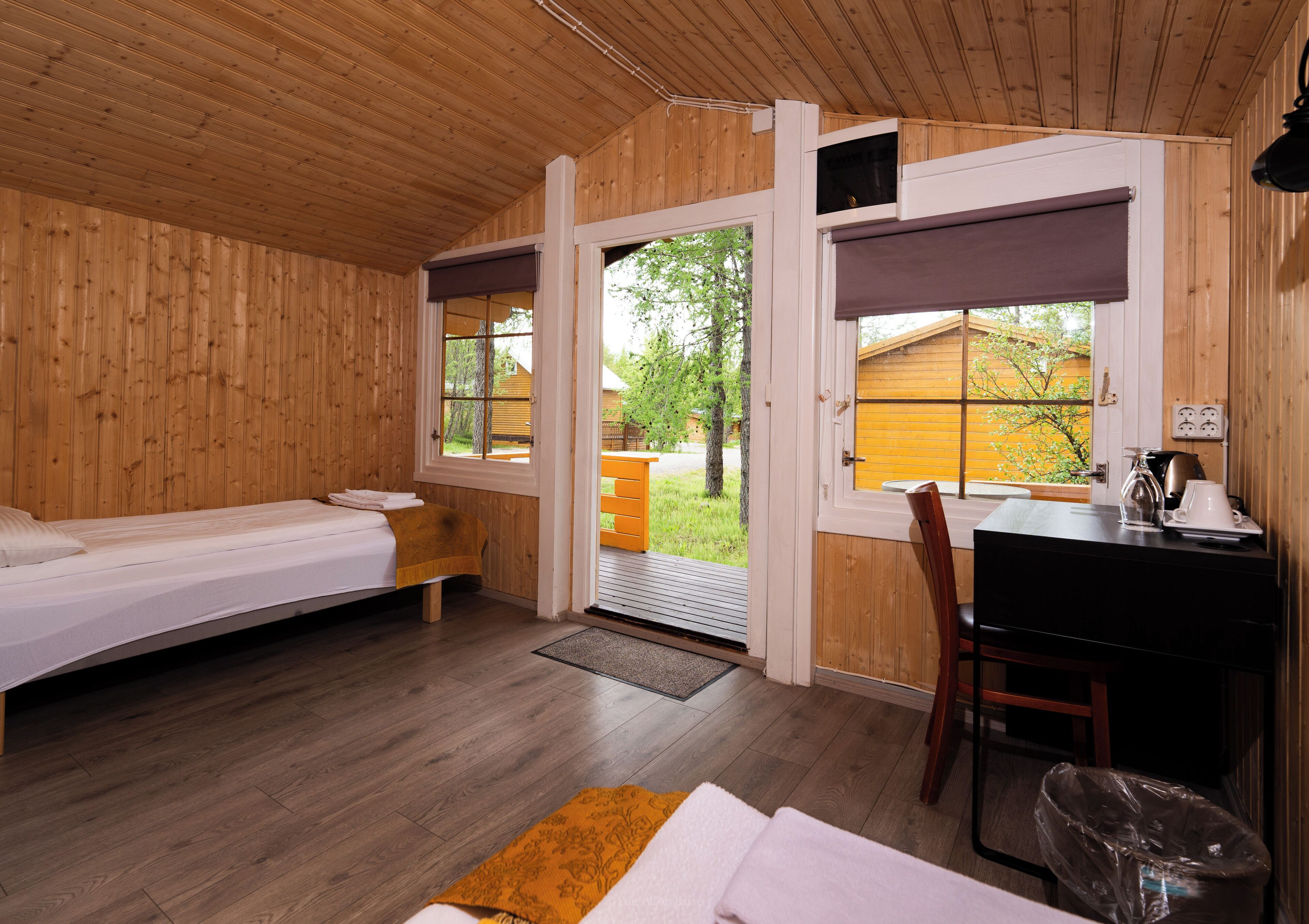 Eine Holzhütte mit einem Bett, einem Schreibtisch und einem Stuhl. Ein Fenster bietet Blick ins Freie.